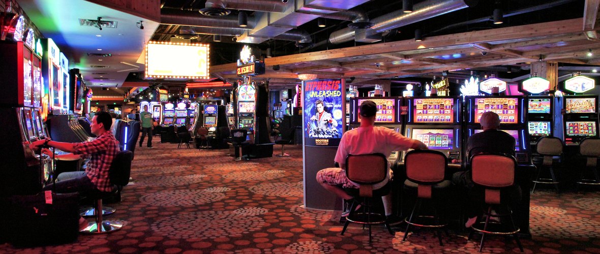 Sala di un casinò con file di postazioni di slot e giocatori seduti